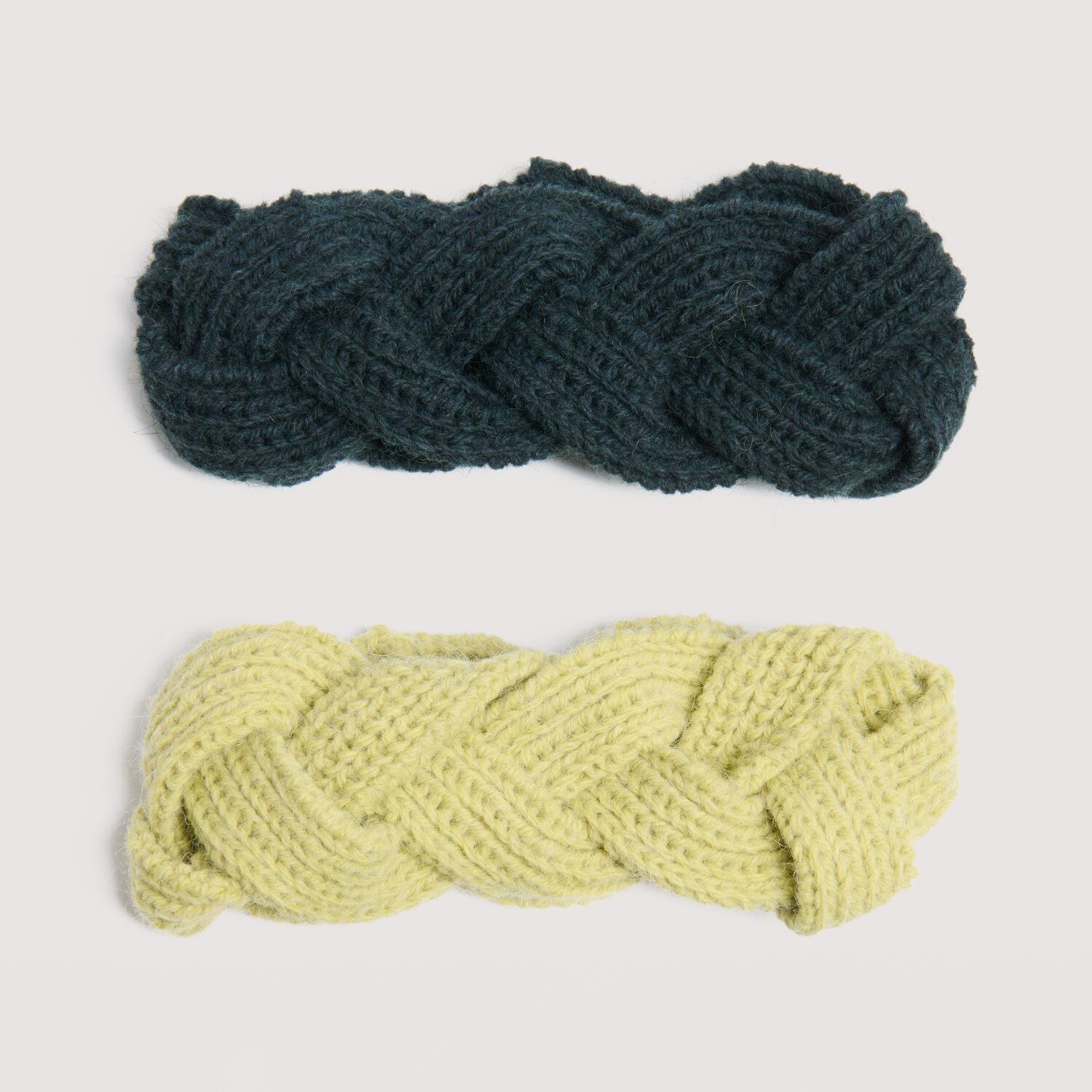 Die Neue Masche No. 16 Herbst zeigt zwei geflochtene Strickstirnbänder von Wolle Rödel, übereinander liegend in dunklem und hellem Ton auf hellem Hintergrund.