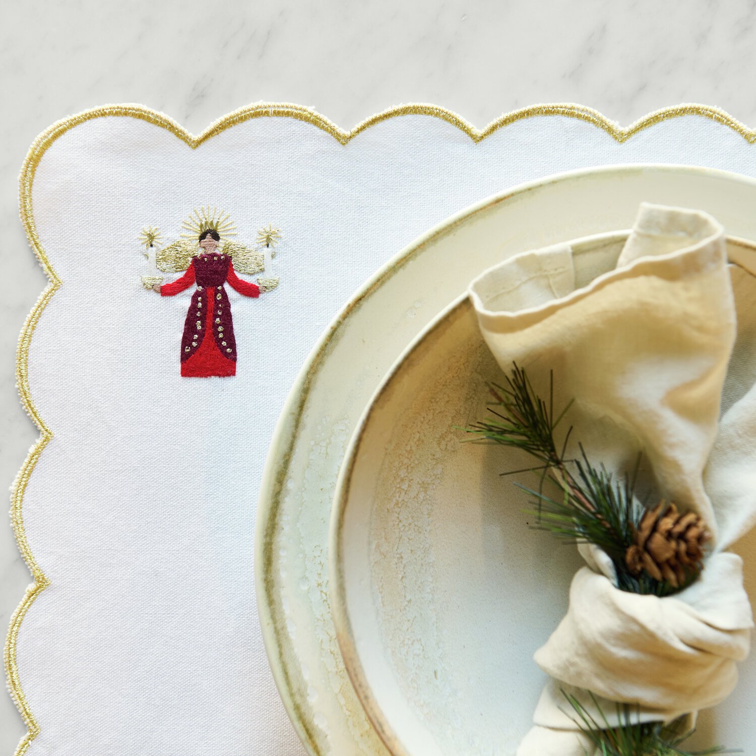 Stick & Stitch Stickpackung Engel mit Kerzen 16 Stück zeigt einen gestickten Engel auf weißem Stoff neben einem dekorierten Teller.