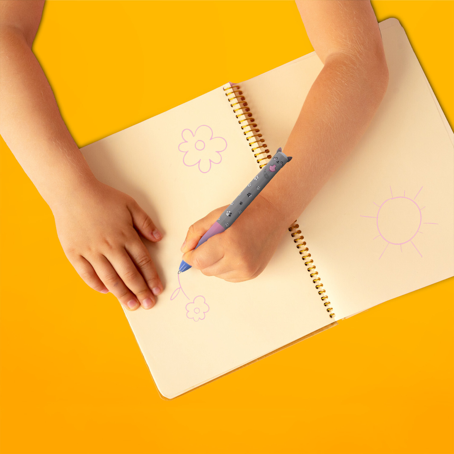 Zweifarbiger Kugelschreiber Click&Clack von Legami in Kinderhand, zeichnet Blumen und Sonne in ein Notizbuch auf gelbem Hintergrund.