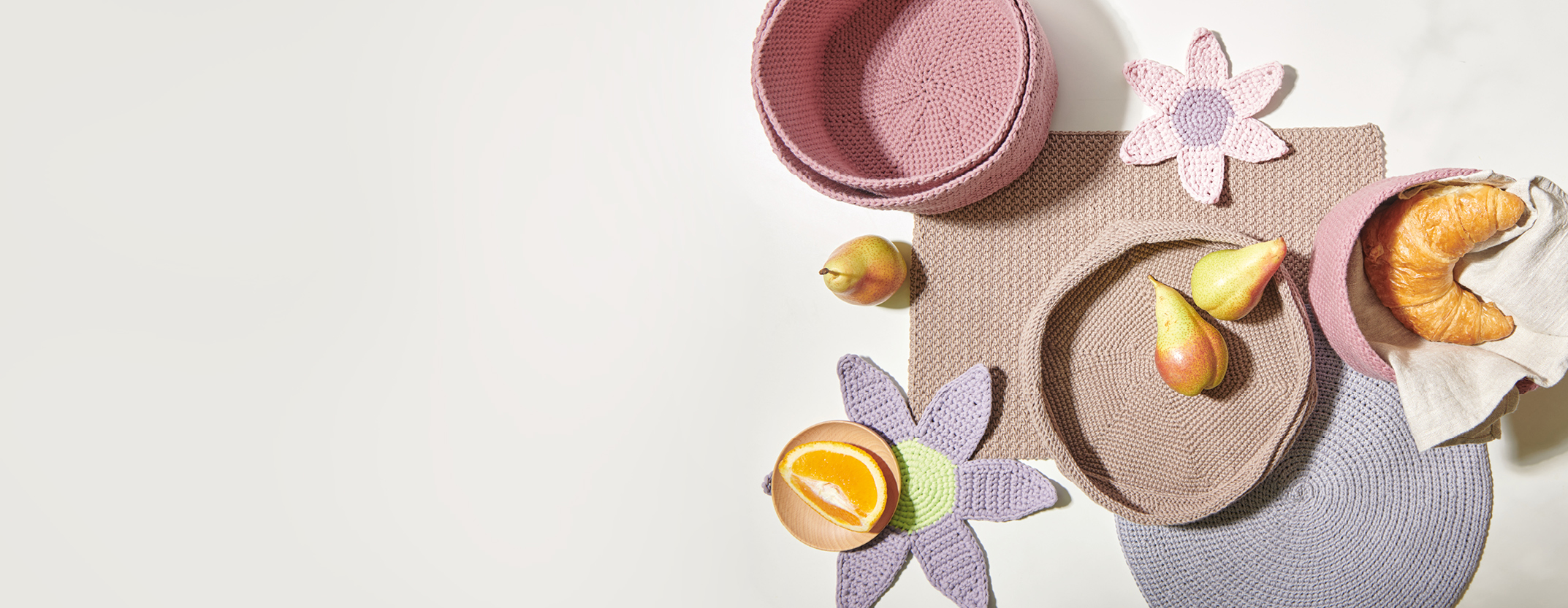 Drei pinke gehäkelte Körbe in unterschiedlichen Größen, eine brauen gehäkelte Schale, gehäkelte Tischsets und Blumenuntersetzer. Flatlay von Produkten.
