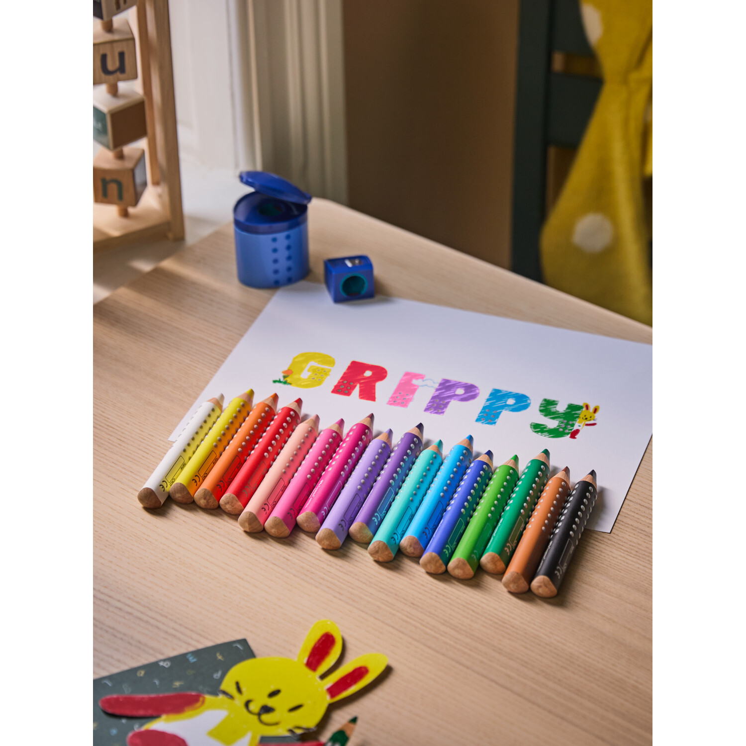 Buntstift Grippy, farbenfrohe Stifte auf Tisch mit blauer Spitzdose, ideal für kreatives Zeichnen.