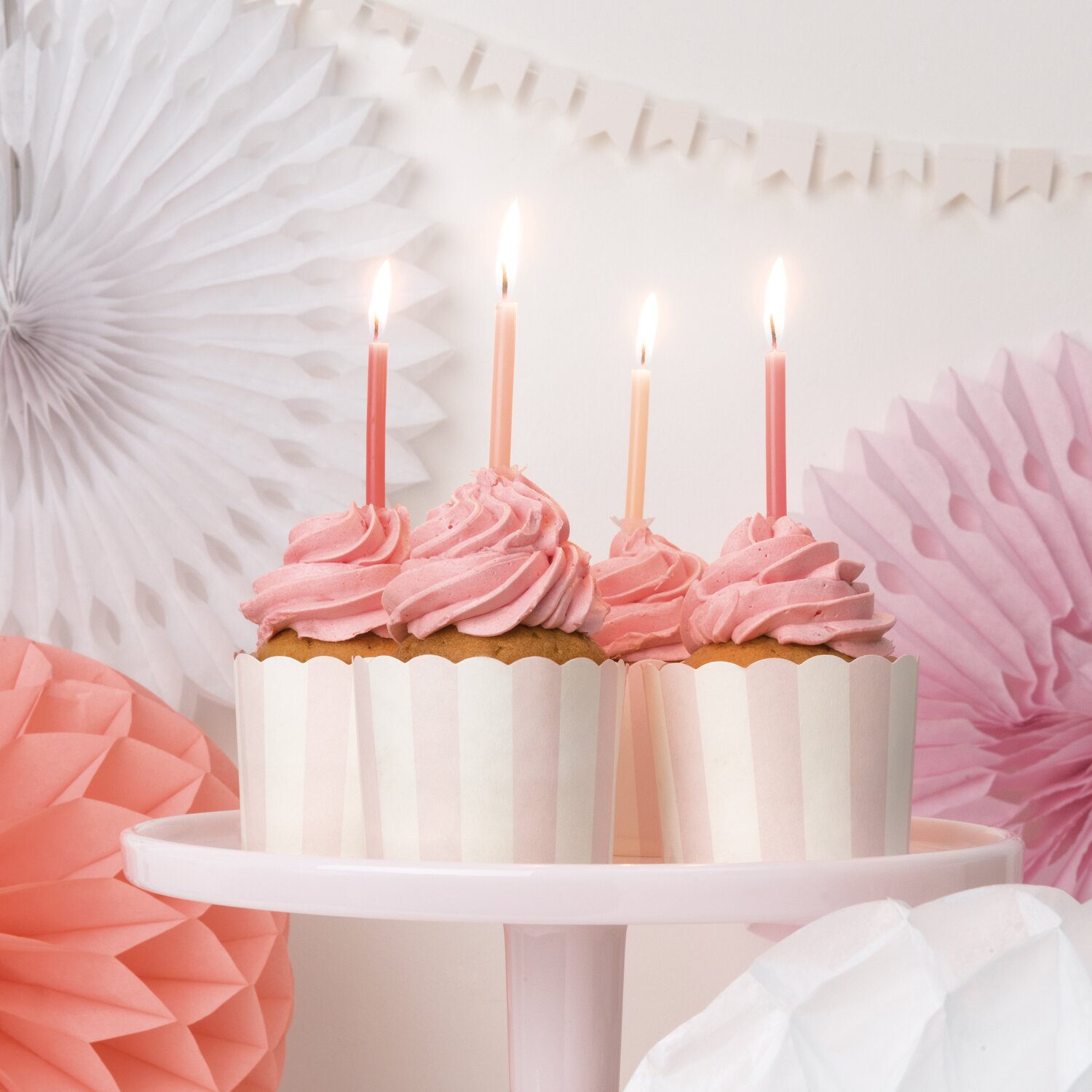 Kerzenset Fashion zeigt 48-teiliges Zubehör von Rico Design mit farbigen Kerzen auf rosa Cupcakes vor zarten Deko-Fächern für stilvolle Partydekoration