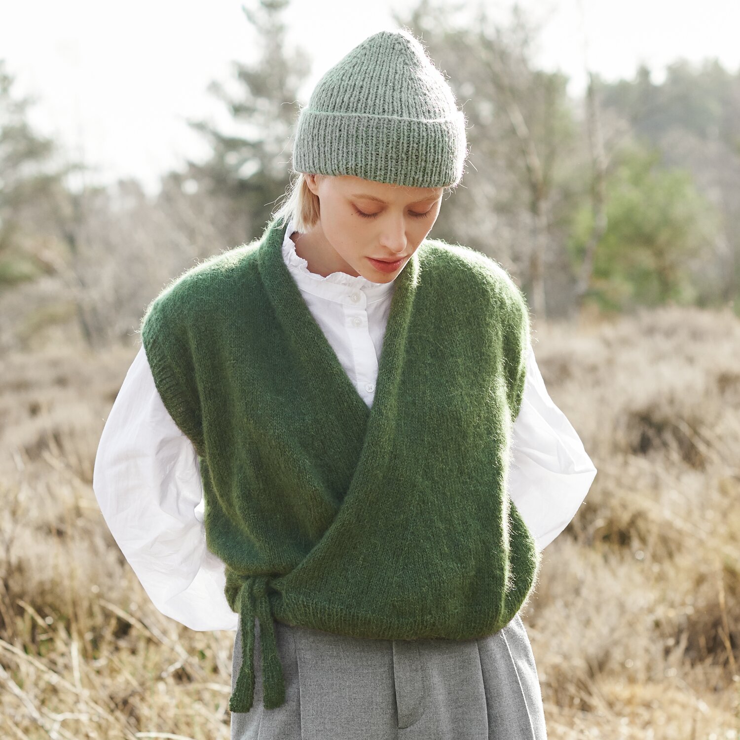 Strickset Weste Modell 14a aus Lovewool No. 21 von Rico Design Strickset Weste Modell 14a aus Lovewool No. 21: Frau in grüner Weste und grauer Mütze in natürlicher Umgebung.