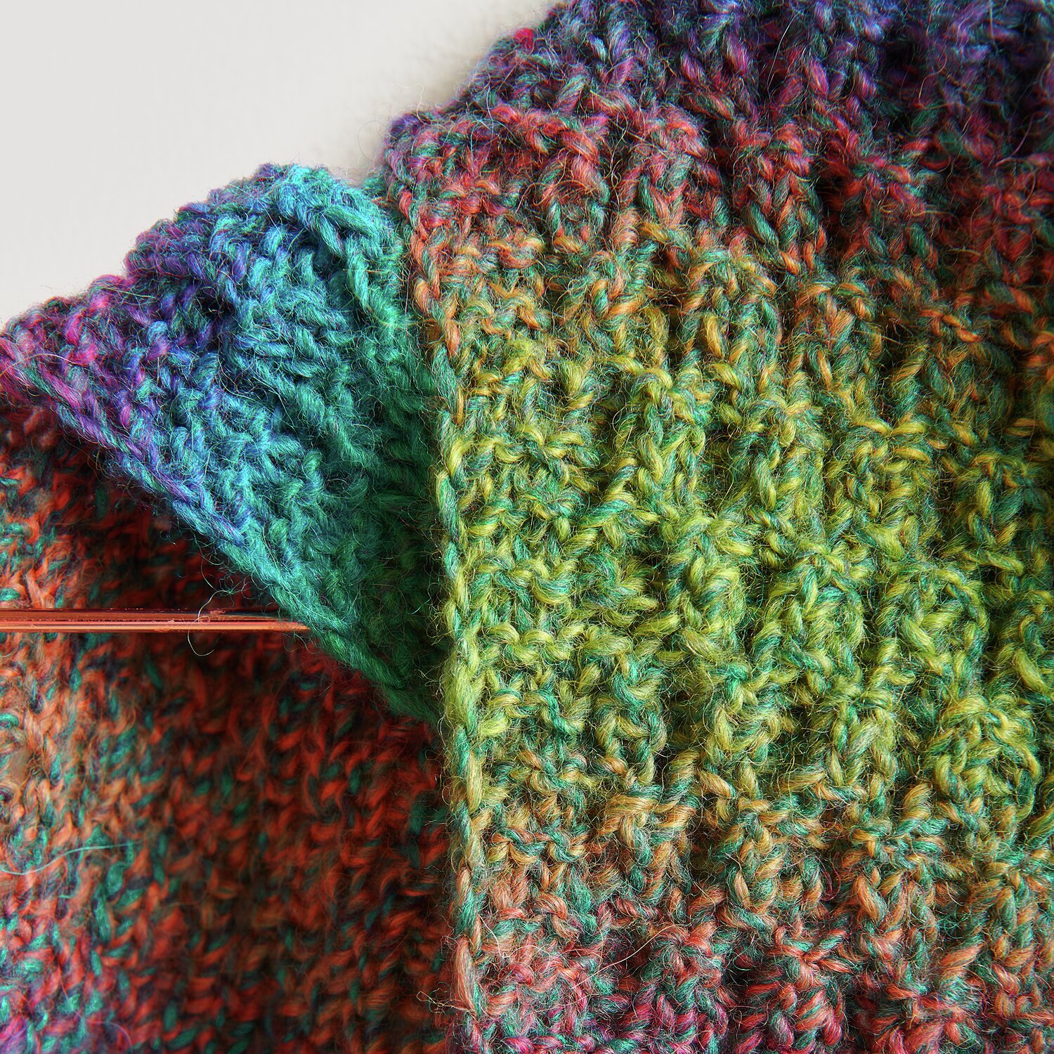 Die Neue Masche No. 13 Herbst von idee. Creativmarkt Creative Melange Alpaca Wonderball dk zeigt ein gestricktes, buntes Textil mit Stricknadel.