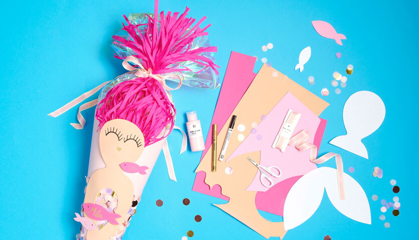 Bastelanleitung Meerjungfrauen-Schultüte: Bunte Materialien und Werkzeuge auf blauem Hintergrund für kreatives Basteln.