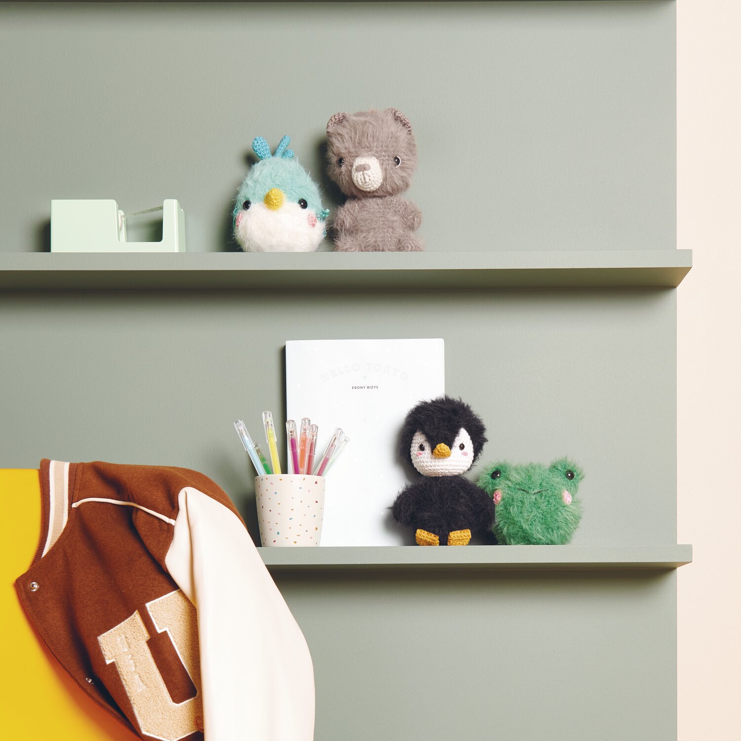 Creative Ricorumi dk 25g Farbe Tanne von Rico Design Ricorumi Furry Animals auf einem Regal mit Stiften und Jacke. Farben: Türkis, Schwarz, Grün.