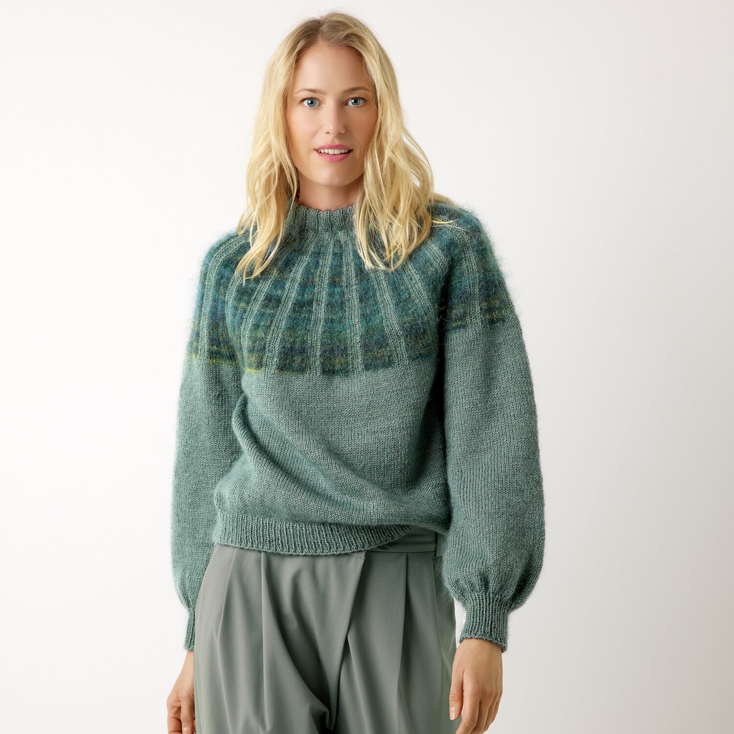 Strickset Pullover Modell 27 aus Die Neue Masche No. 13 von idee. Creativmarkt Strickset Pullover Modell 27 aus Die Neue Masche No. 13: Frau trägt blauen Pullover mit Rundhalsausschnitt und weiten Ärmeln, kombiniert mit grauer Hose.