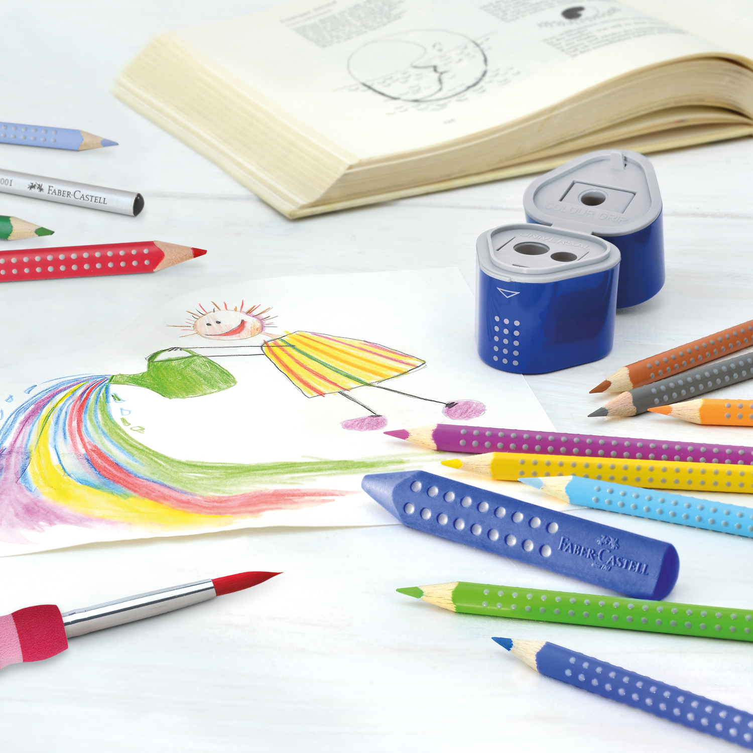Colour Grip 2001: Buntstifte und Anspitzer von Faber Castell auf einem Tisch mit Kinderzeichnung.