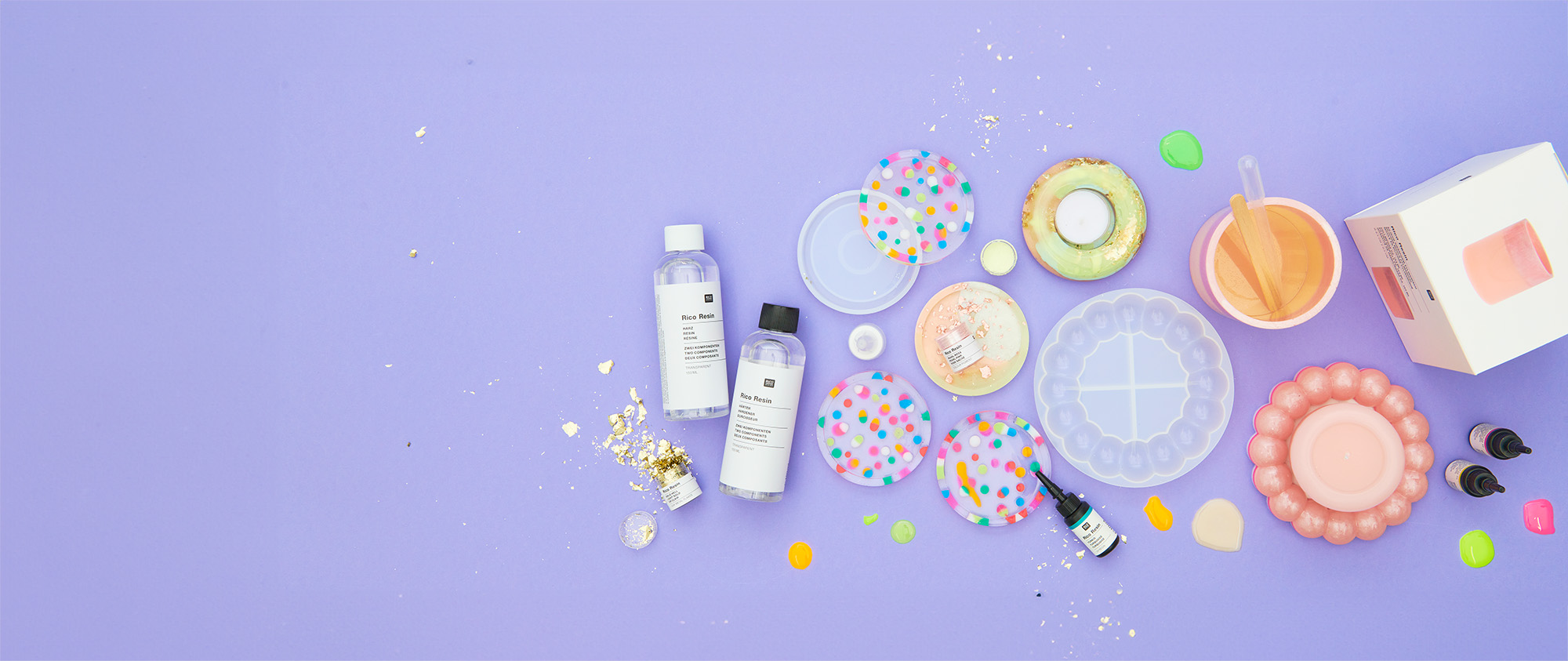 Flaschen mit buntem und transparentem Resin, Silikonformen, Farbpigmente und Blattmetall, sowie weiteres Zubehör zum Resin gießen und fertig gegossene Untersetzer. Flatlay von Produkten.