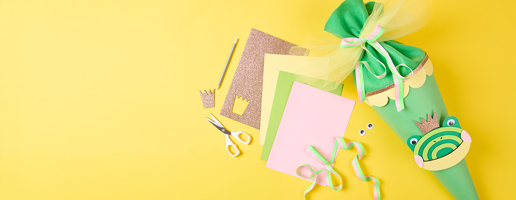 Grüne Schultüte neben Papier und Bastelmaterial. Flatlay von Produkten.