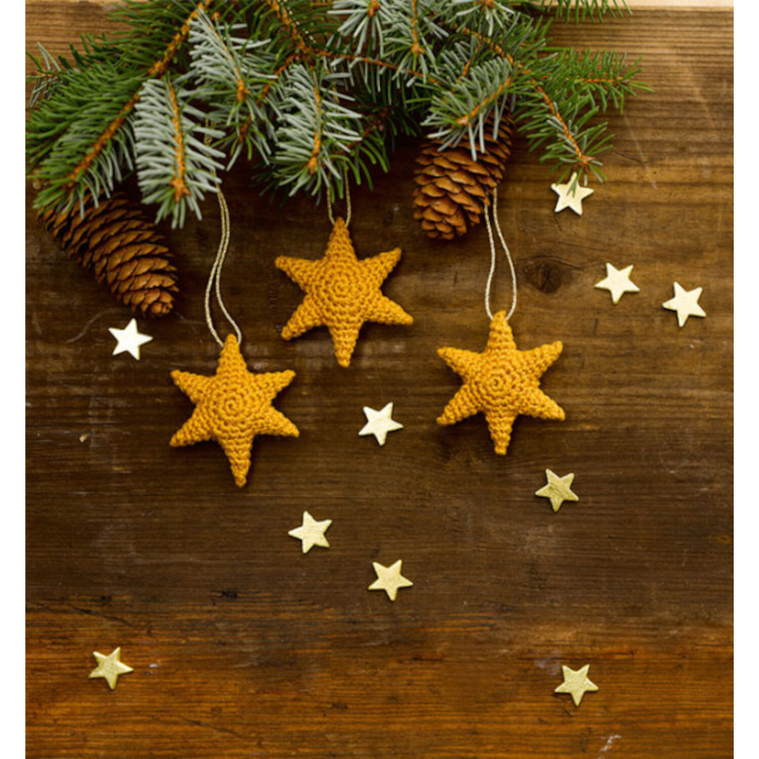 Christmas Cuteness. Drei gehäkelte Sterne als Baumschmuck vor Tannenzweigen und Zapfen.