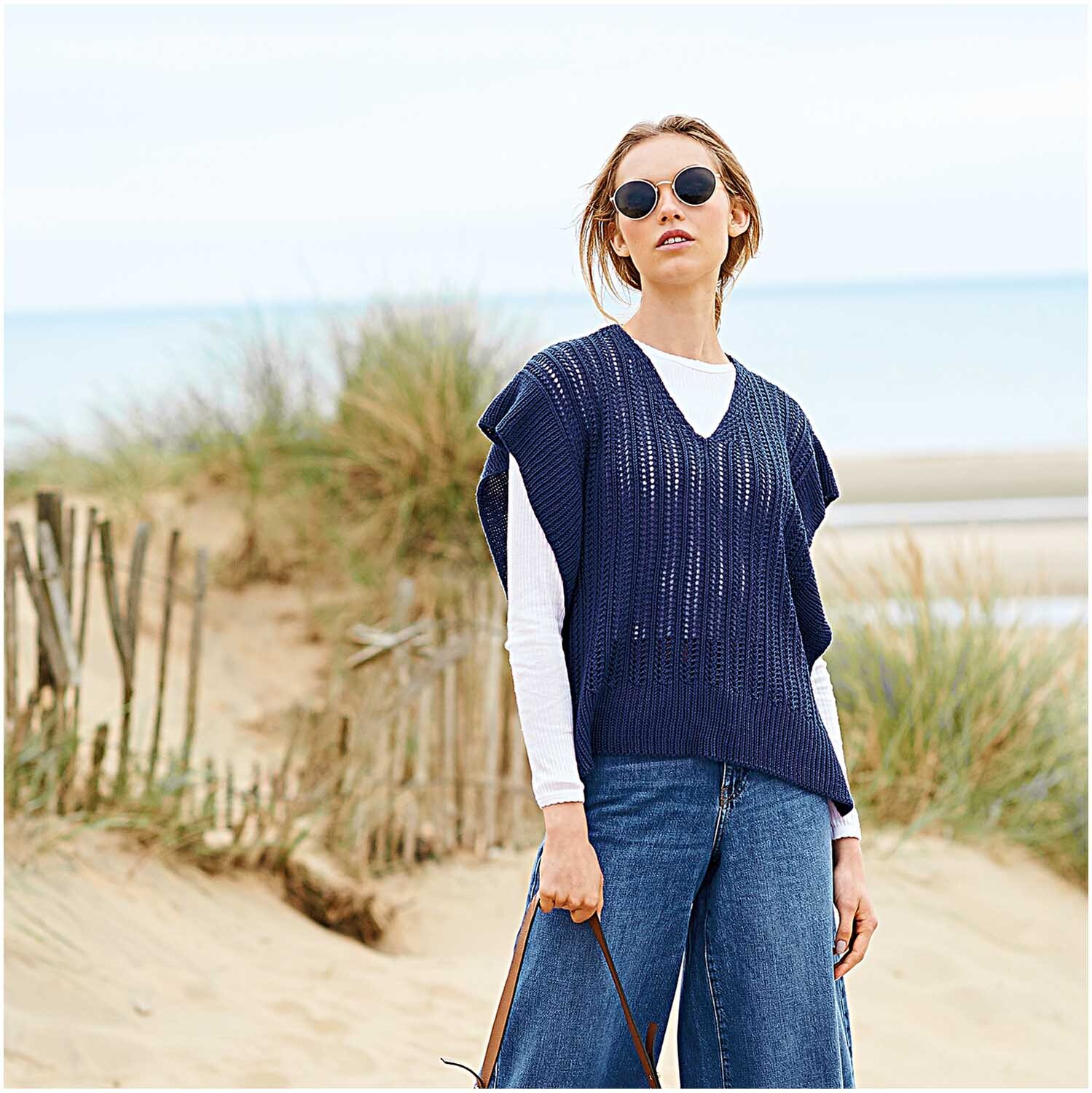 Creative Silky Touch dk: Frau am Strand in marineblauem Strickoberteil, kombiniert mit Jeans und Sonnenbrille.
