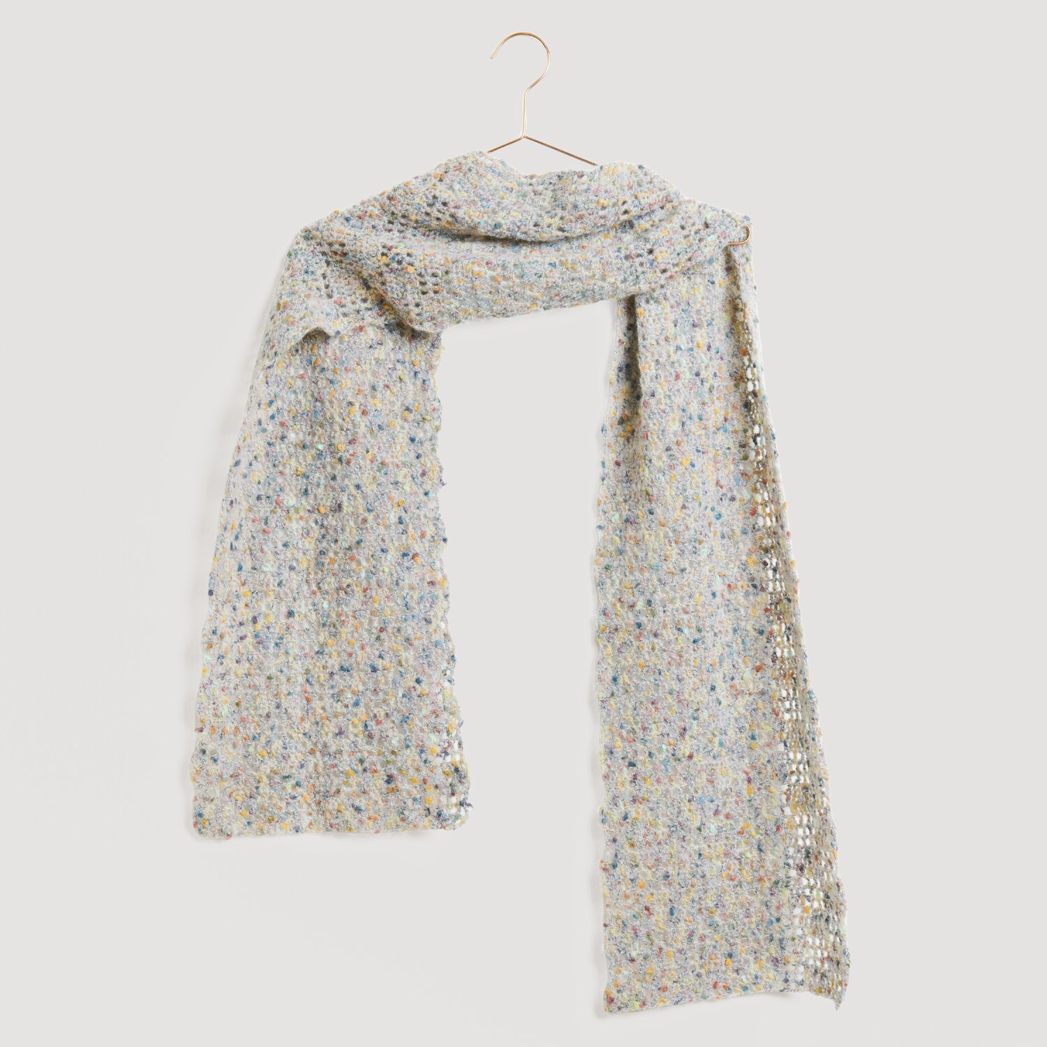 Lovewool No. 21 Herbst-Winter Sprachauswahl deutsch von Rico Design Ein eleganter, hellgrauer Schal mit bunten Akzenten, aufgehängt an einem goldenen Haken. Marke: Modell Legeware. Perfekt für stilvolle Outfits und vielseitige Kombinationen.