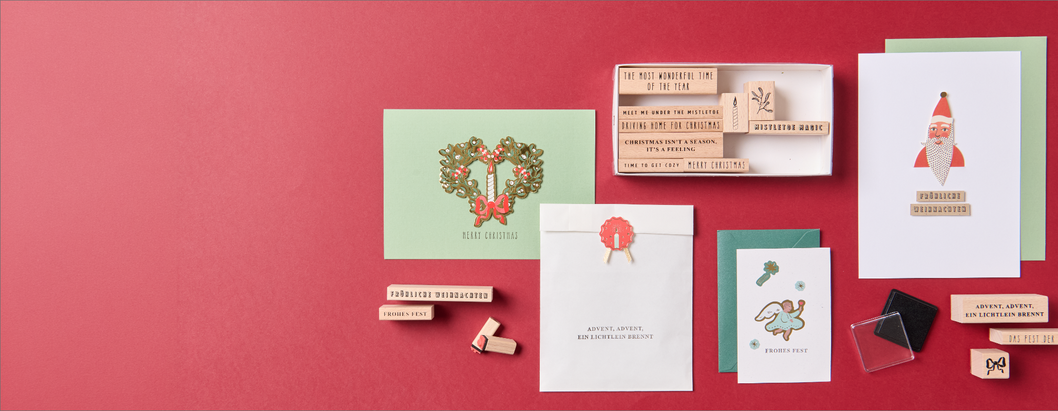 Weihnachtliches Bastelset mit Grußkarten, Stempeln, Holzbuchstaben und Bastelzubehör auf rotem Hintergrund.