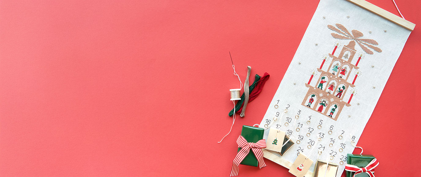 Ein Adventskalender mit einer Lichterpyramide und Zahlen bestickt, sowie kleinen Ringen an welchem Geschenke hängen. Flatlay von Produkten.
