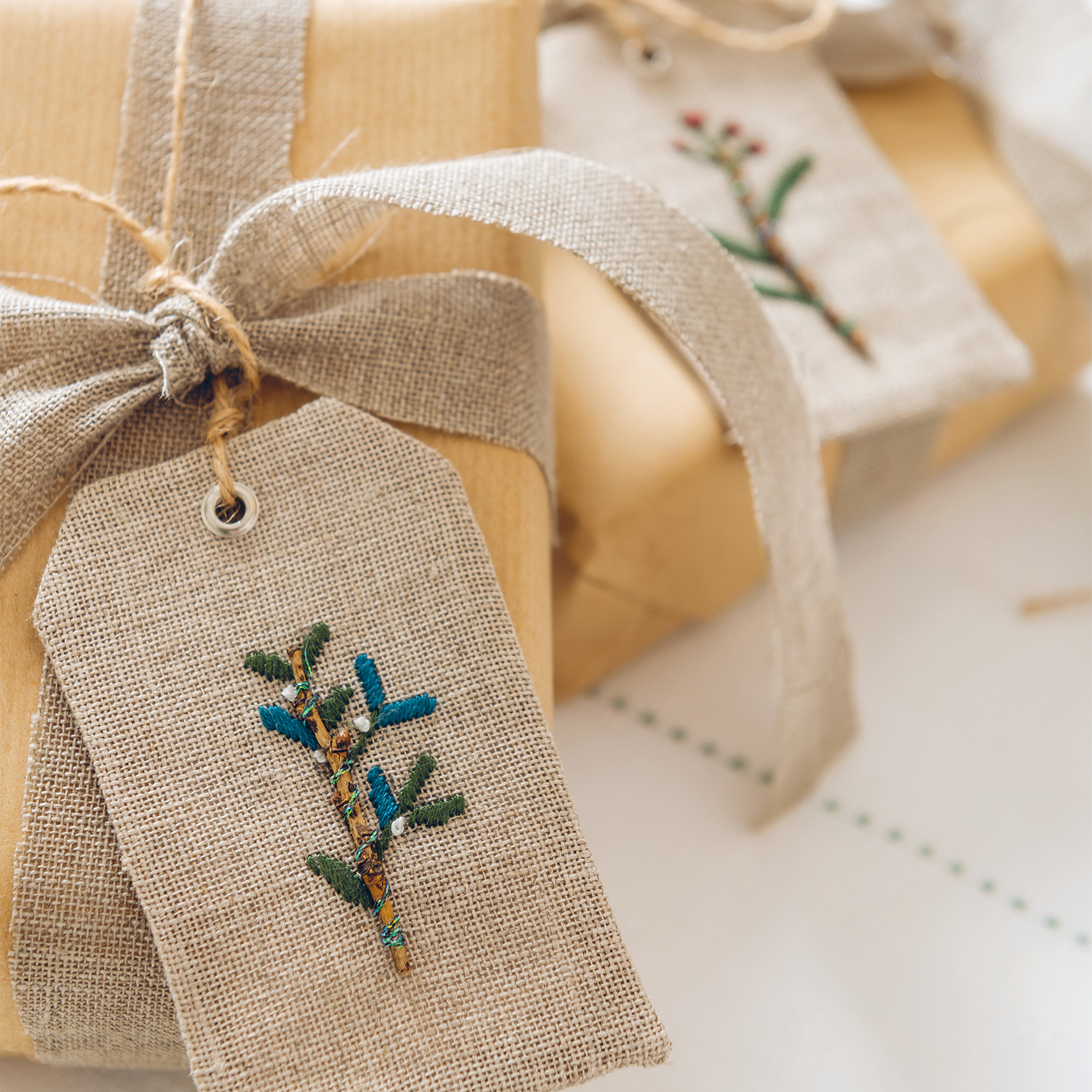 Stickanleitung Geschenkanhänger für Weihnachten: Handgemachte Anhänger mit Stickerei auf Leinen, dekoriert mit Zweigen, ideal für festliche Geschenke.