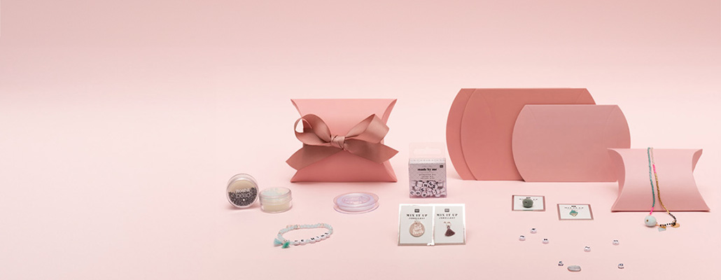 Geschenkschachteln mit Schmuckperlen, -band und -anhänger. Mehrere pinke Geschenkschachteln mit Schmuckperlen, Schmuckband und verschiedenen Anhängern. Fotosetting rosa Wand.
