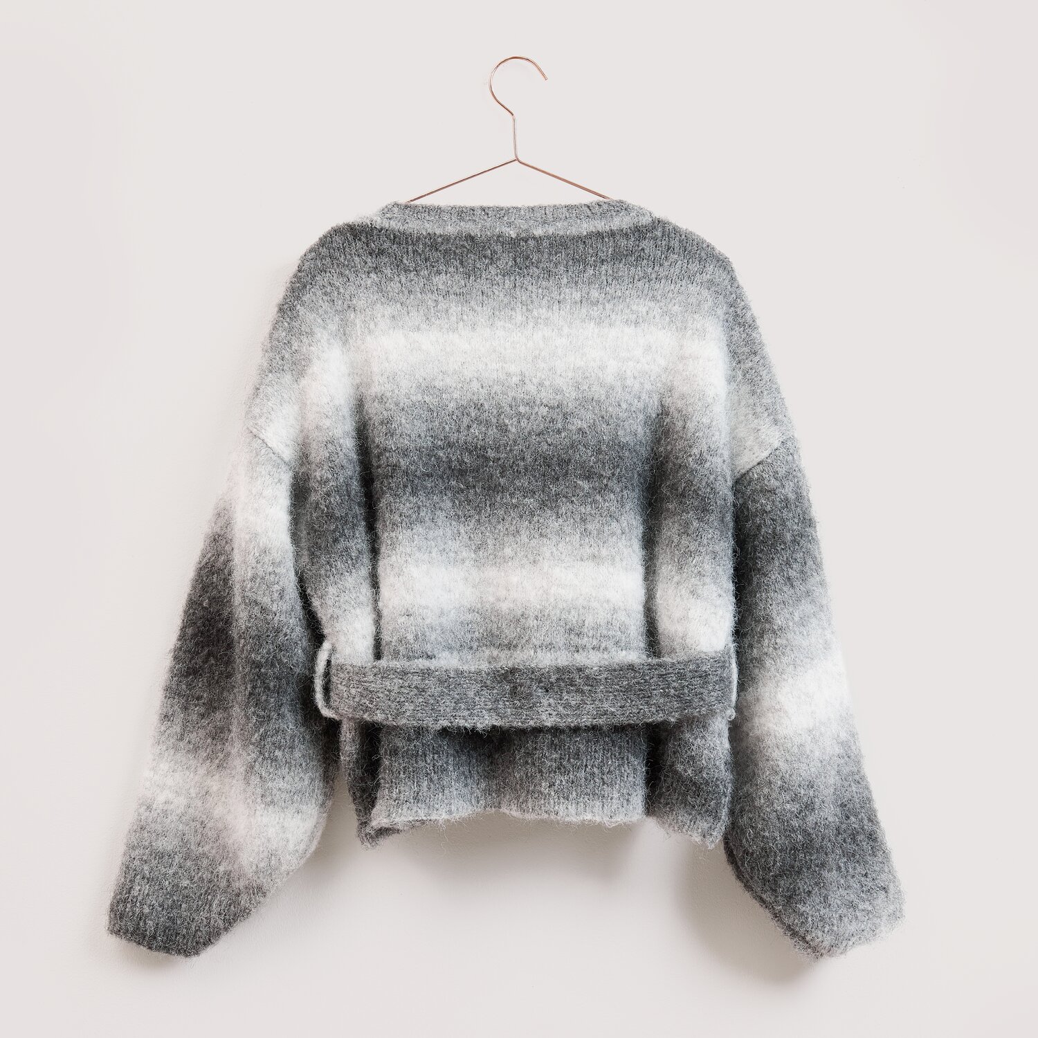 Die Neue Masche No. 16 Herbst Strickjacke von Wolle Rödel, locker geschnitten mit breitem Bindegürtel, weichem Farbverlauf und auf einem Bügel hängend.