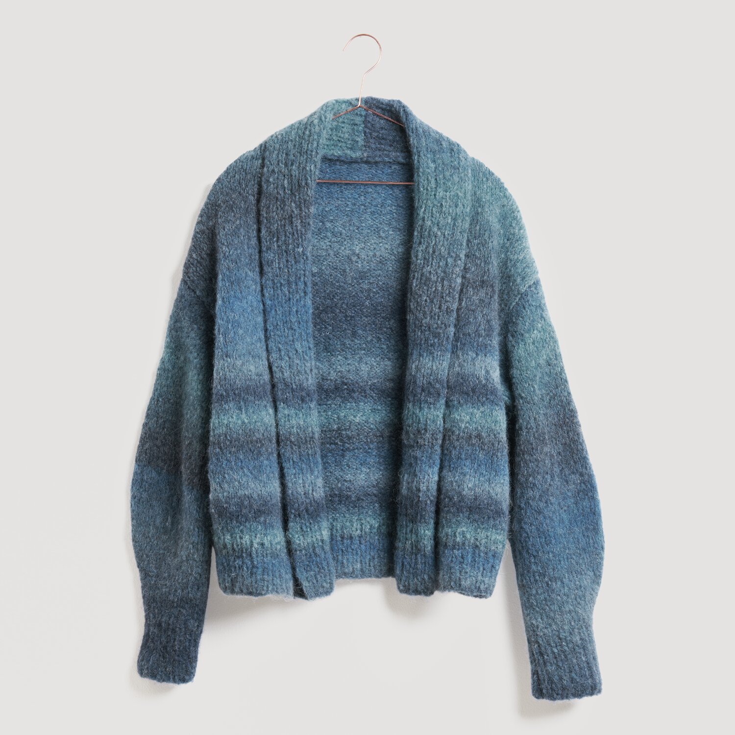 Lovewool No. 21 Herbst-Winter Sprachauswahl deutsch von Rico Design Blauer Strickpullover von Modell Legeware, hängend an einem Kleiderbügel. Der Pullover zeigt ein gestreiftes Muster in verschiedenen Blautönen und hat lange Ärmel. Ideal für kühle Tage.