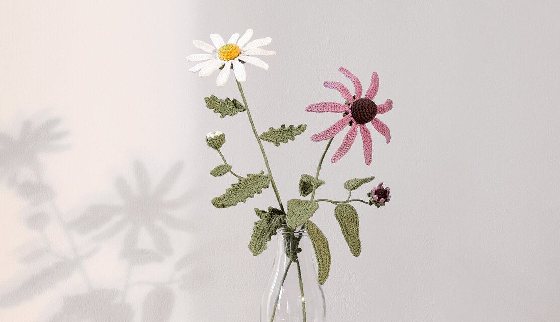 Material Ricorumi In the Meadow Sonnenhut, gehäkelte Wiesenblumen mit grünen Blättern in Glasvase vor heller Wand, dekorative DIY-Ideen für Wohnaccessoires