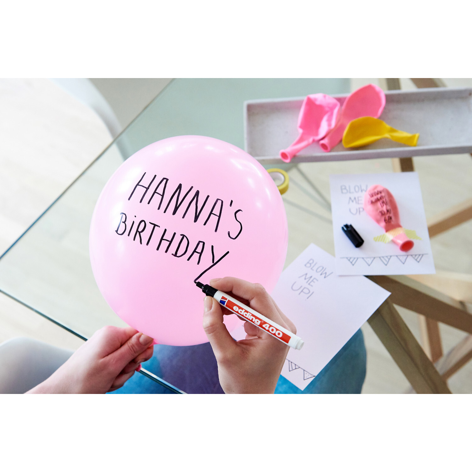 400 Permanentmarker schwarz 1mm von edding International 400 Permanentmarker schwarz 1mm schreibt auf rosa Ballon. edding Stift liegt auf Tisch mit Karten und Luftballons.