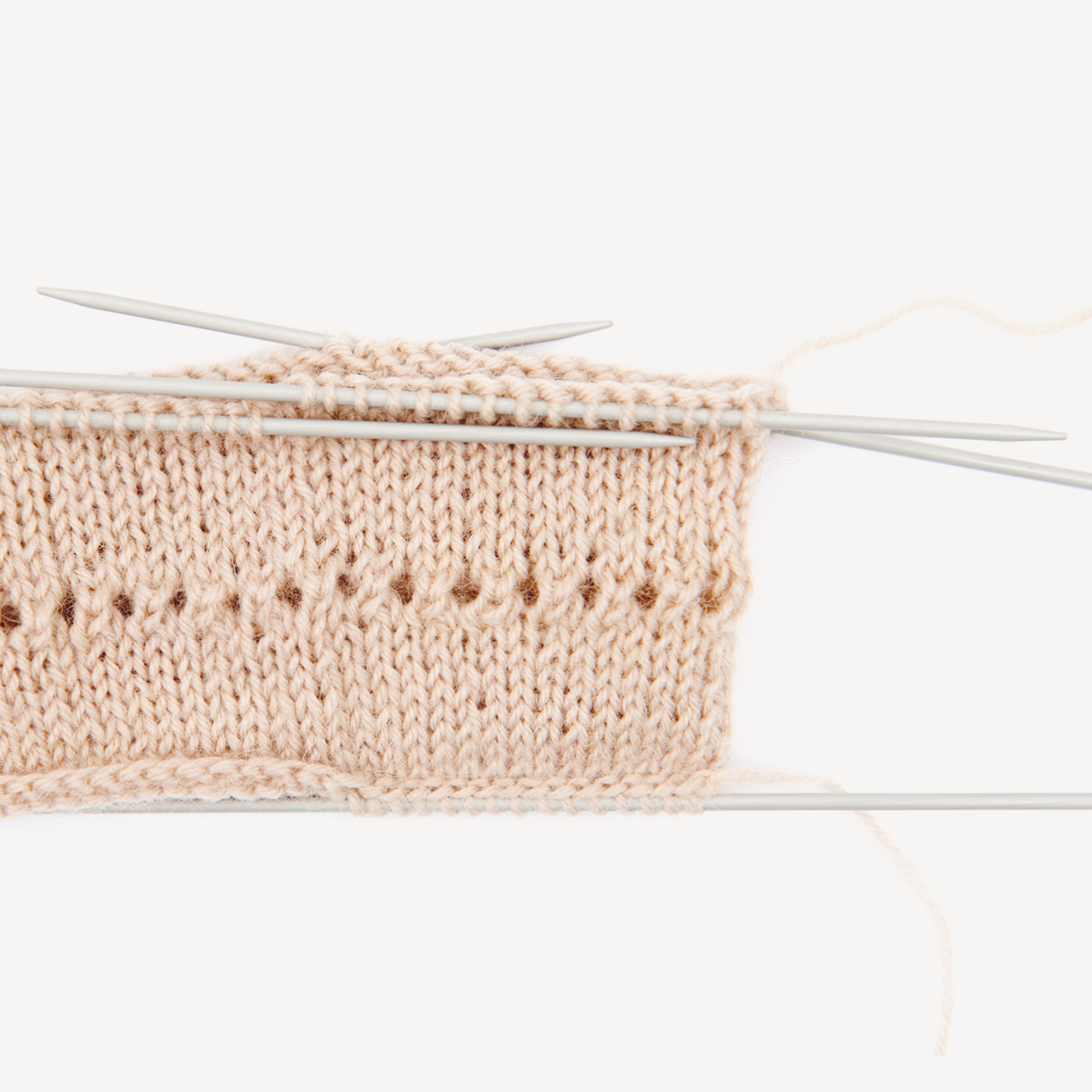 Ein helles Strickstück mit Nadelspiel. Flatlay von Produkten.