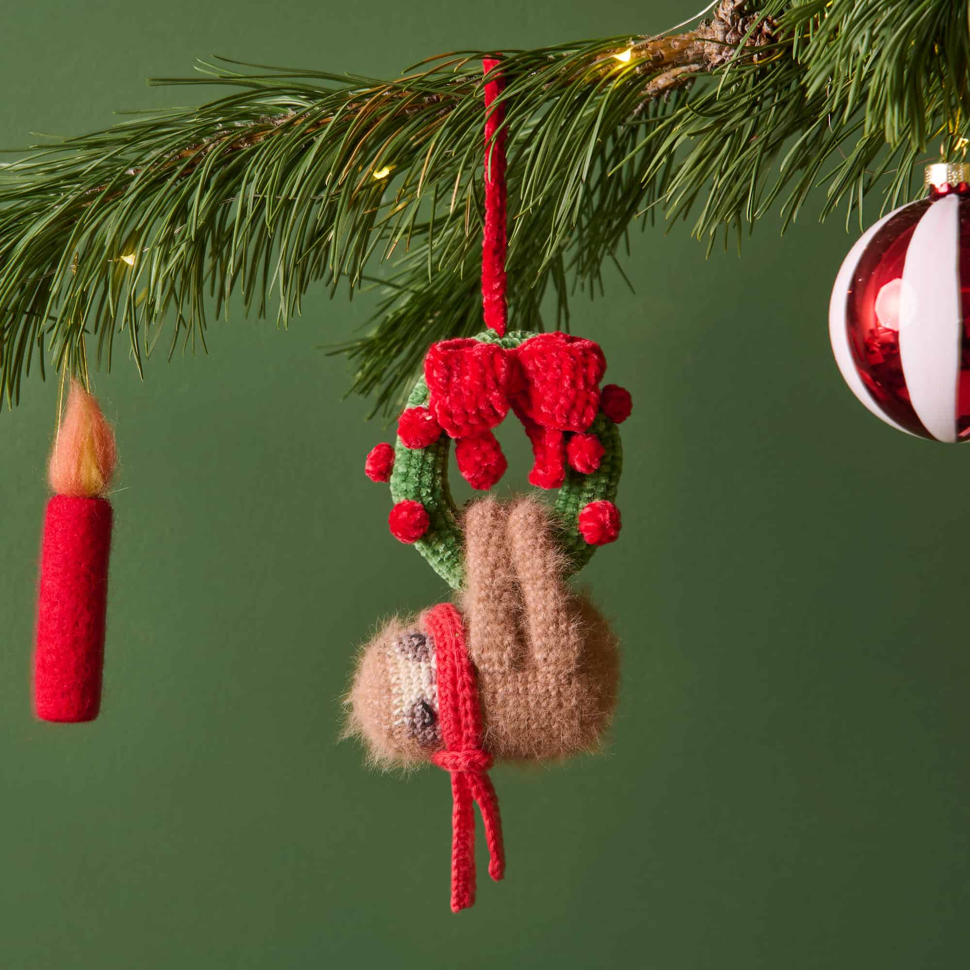 Gehäkelte Figur in Form eines Faultiers ist mit Weihnachtskranz und roter Schleife vor einem weihnachtlich geschmückten Hintergrund platziert.