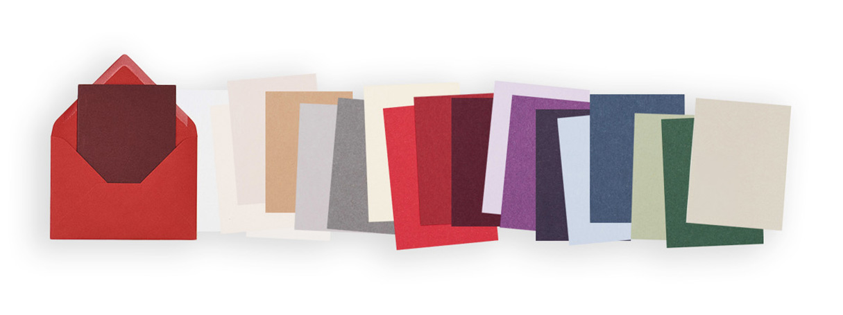 Ein roter Umschlag mit Karte daneben Karten in verschiedenen Farben sortiert. Flatlay von Produkten.