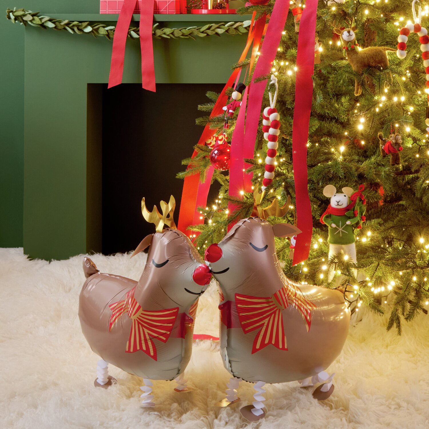 Folienballon Rentier laufend vor festlich geschmücktem Weihnachtsbaum mit Lichtern und Geschenken.