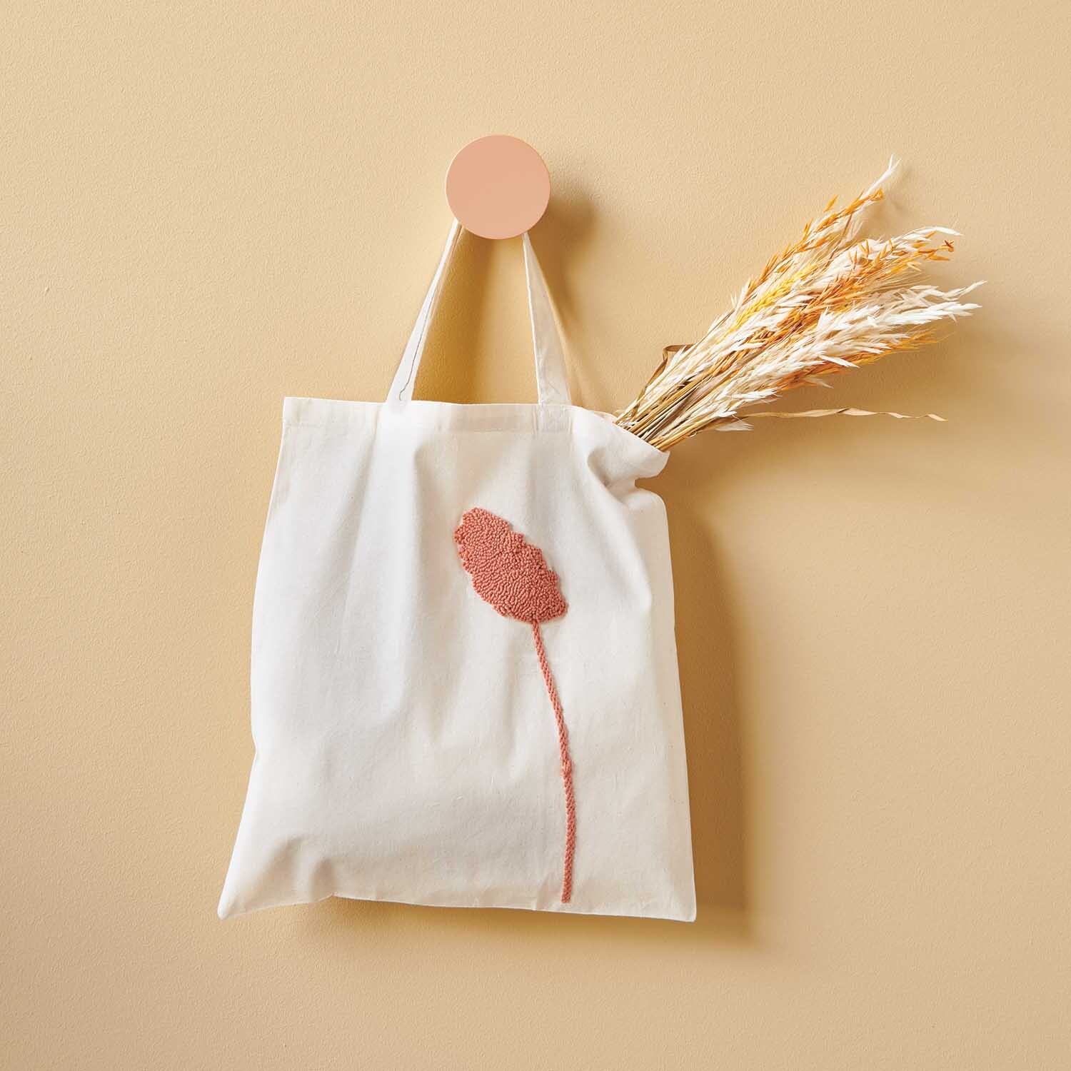 Anleitung Jutebeutel mit der Punch Needle gestalten: Weißer Beutel mit rosa Blumenstickerei, dekoriert mit Trockenblumen.