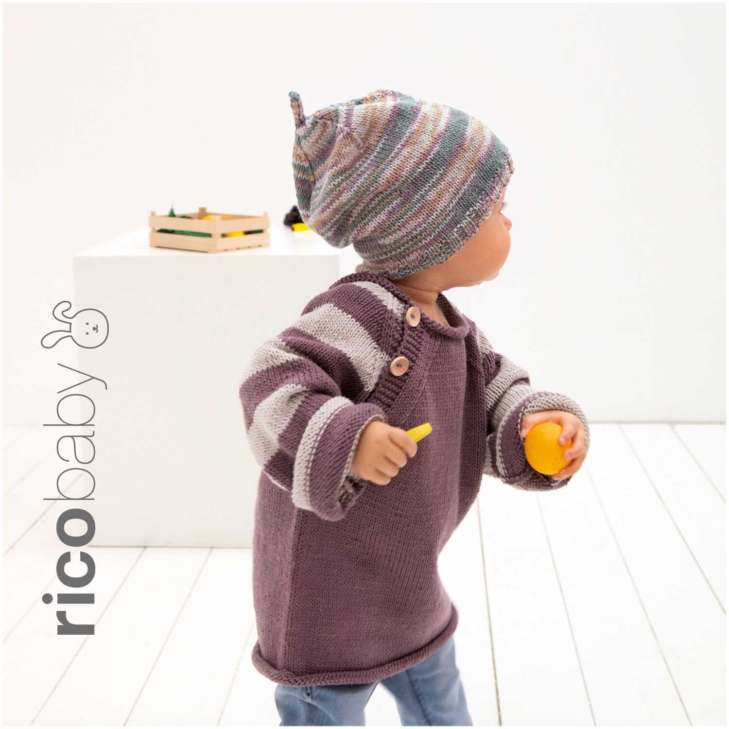 Rico Baby Cotton Soft Print dk: Kind in gestricktem Pullover und Mütze, spielt mit Spielzeug.