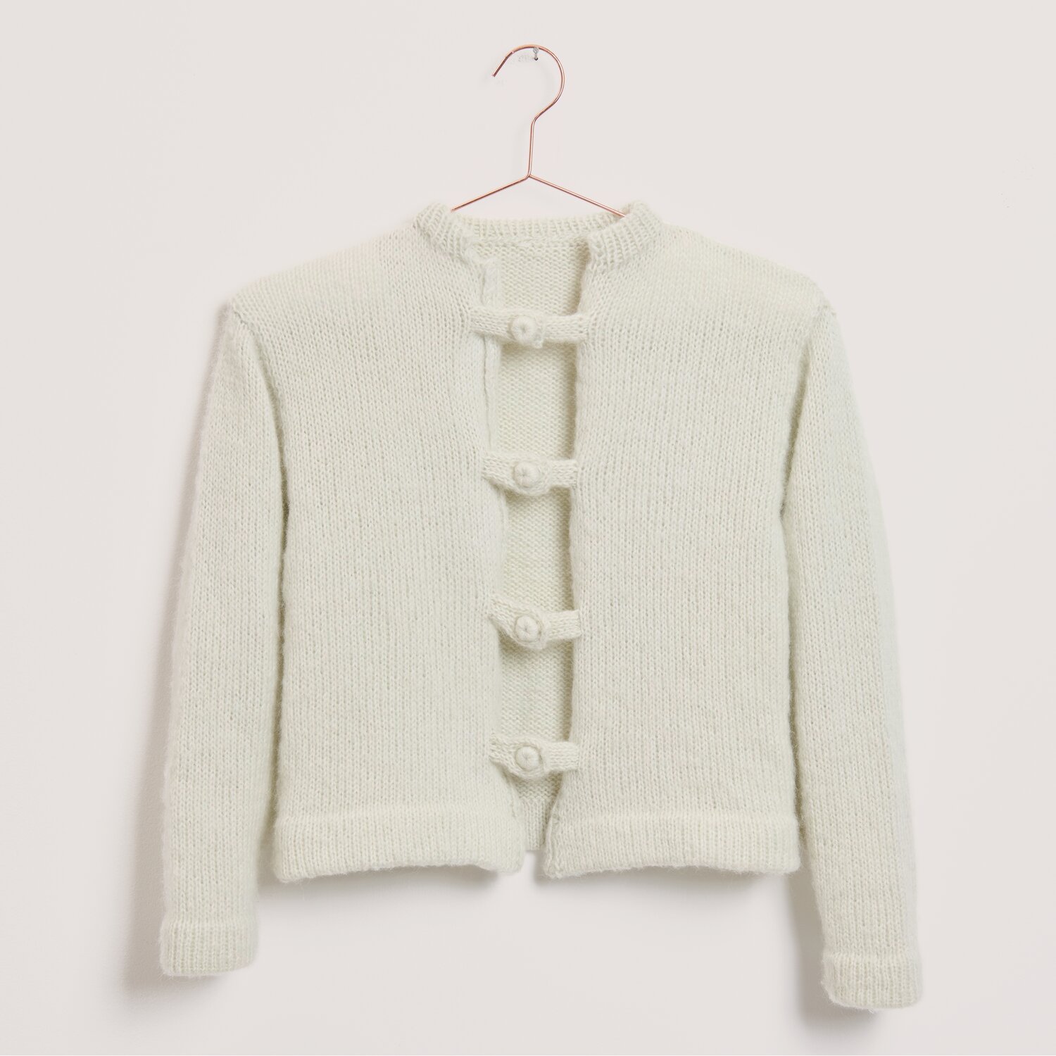 Luxury Merino Alpaca Dream aran, Rico Design, Strickjacke aus weichem Garn in zartem Ton, mit vier markanten Knebelknöpfen, 50g 125m, auf Bügel präsentiert