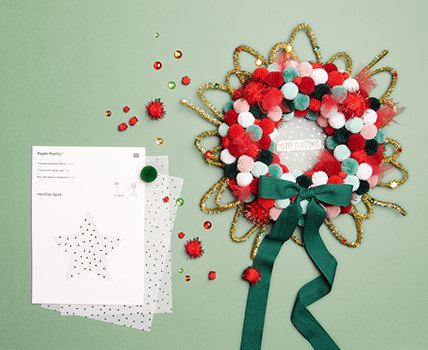 Ein weihnachtlicher Türkranz bestehend aus roten und grünen Pompons mit einer Schleife und Transparentpapier verziert. Fotosetting grüner Hintergrund.