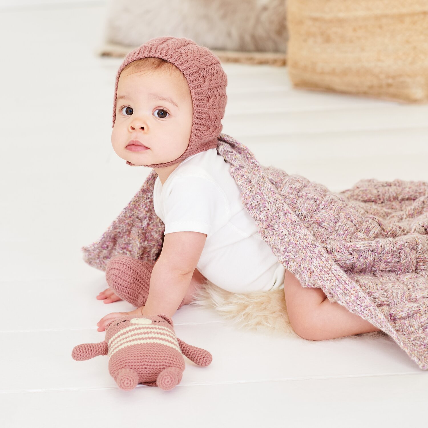 Strickset Mütze Modell 09a aus Baby 044, Strickset Decke Modell 10 aus Baby 044, Baby auf hellem Boden mit gestrickter Mütze, Decke und Kuscheltier in Rosa
