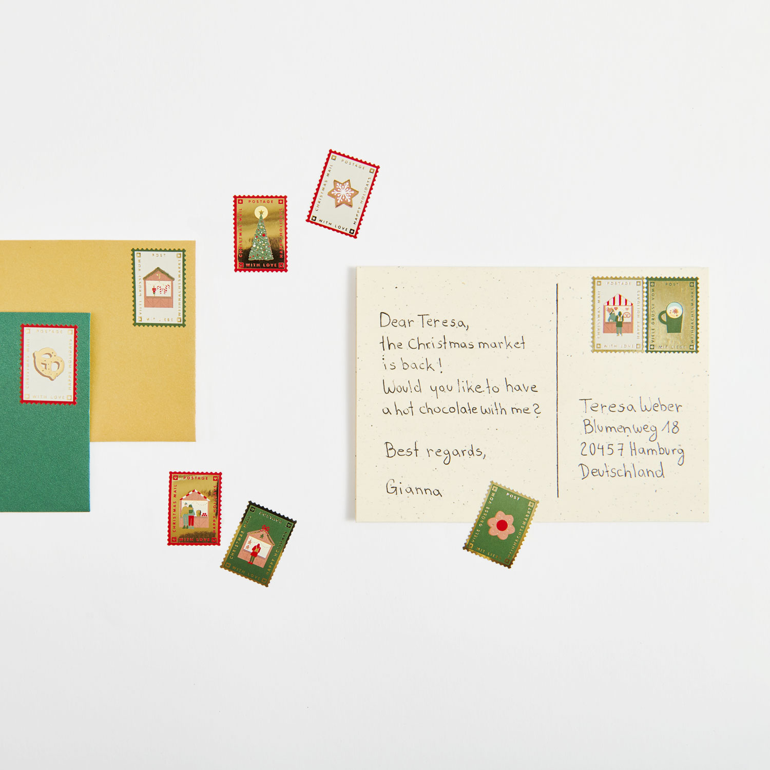 Eine beschriebene Postkarte und zwei Umschläge mit Stickern in Briefmarken Format. Flatlay von Produkten.