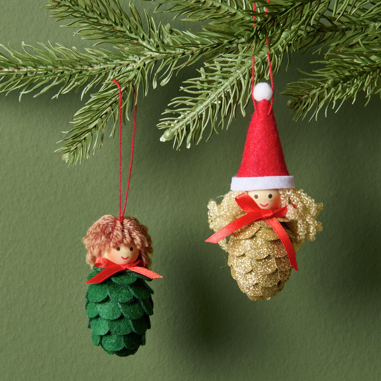 Aufhänger Filz-Zapfenkind mit Mütze Gold und Grün, dekorativ an einem Tannenzweig hängend.