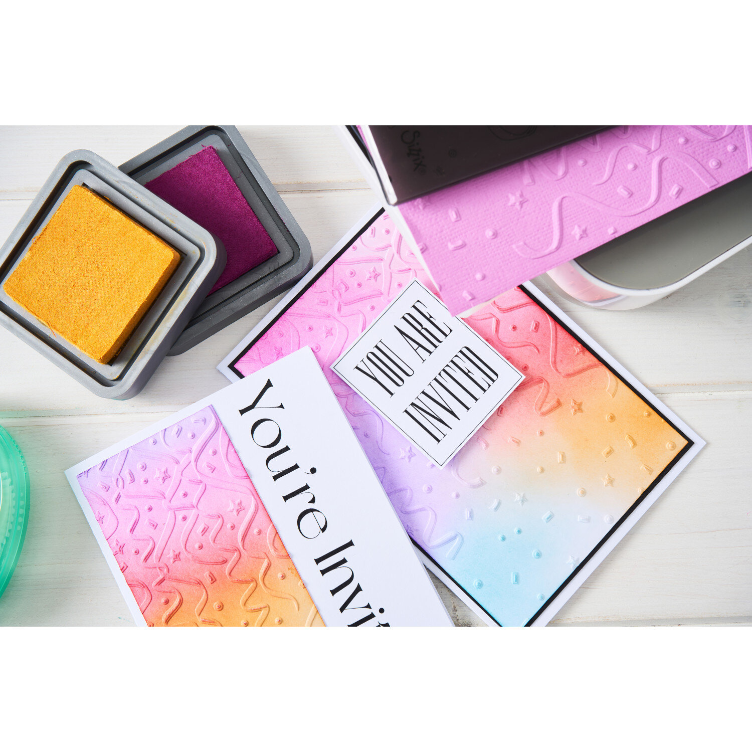 Sizzix Embossing Folder Party Time, Prägeschablone für bunt gestaltete Einladungskarten mit Konfetti- und Luftschlangenstruktur, liegend auf kreativem Basteltisch