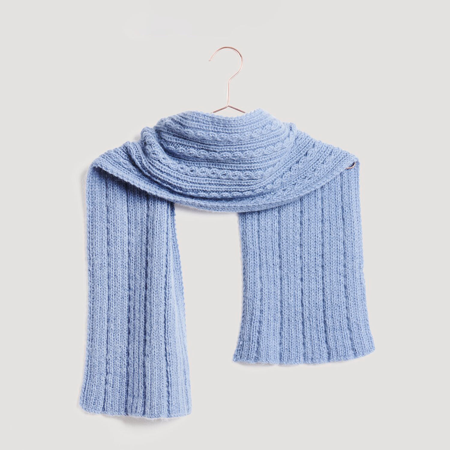 Strickset Schal Modell 29 aus Lovewool No. 21 von Rico Design Stirnband und Schal in hellblauer Strickoptik, präsentiert auf einem Kleiderbügel. Marke: Modell Legeware. Perfekt für kalte Tage, stilvoll und warm.