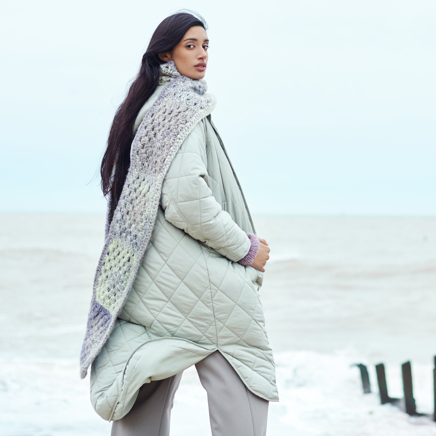 Häkelset Schal Modell 17 aus Lovewool No. 21 von Rico Design Häkelset Schal Modell 17: Frau am Strand mit grauem Schal aus Lovewool No. 21 und Steppmantel.