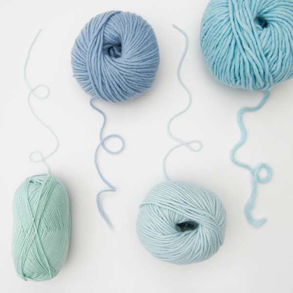 Vier unterschiedliche blaue Knäule mit ausgelegtem Faden. Flatlay von Produkten.