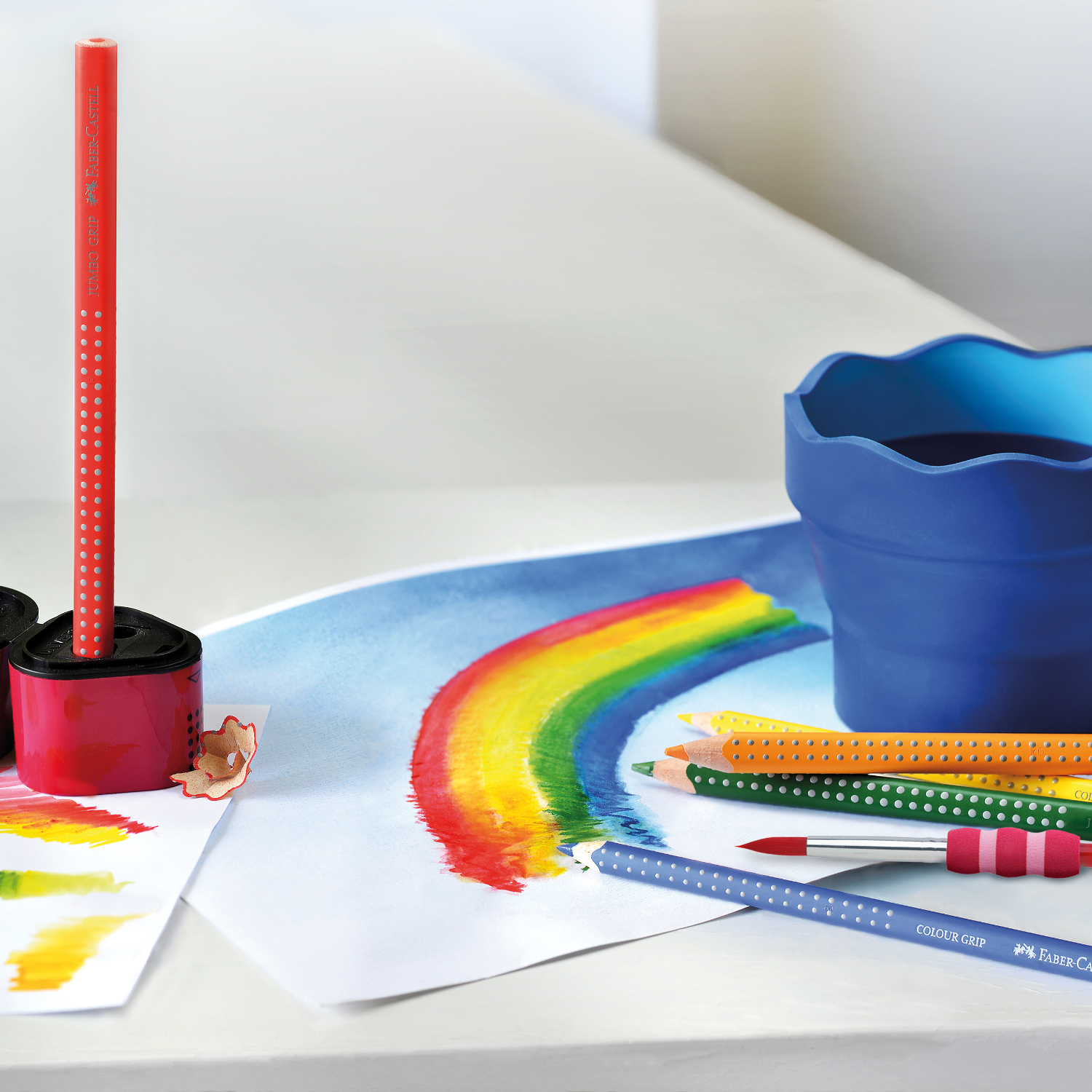 Jumbo Grip Farbstift in Kobaltblau von Faber Castell liegt auf einem Tisch mit buntem Regenbogenbild.