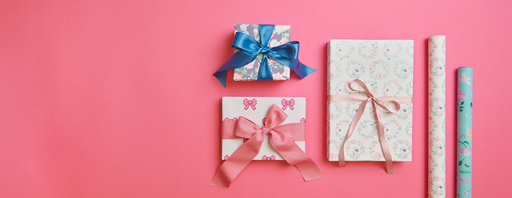Drei verpackte Geschenke mit Schleife neben zwei Geschenkpapierrollen. Flatlay von Produkten.