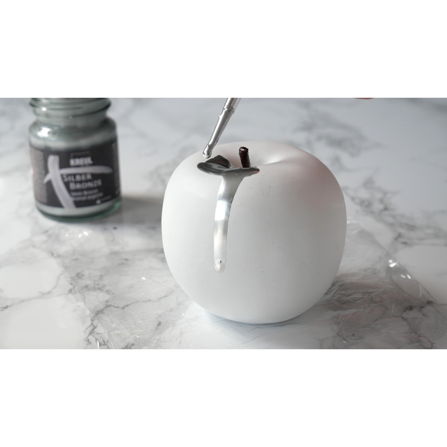 Metallpigmentlack Bronze: Ein weißer Apfel wird mit silberner Farbe von KREUL bemalt.
