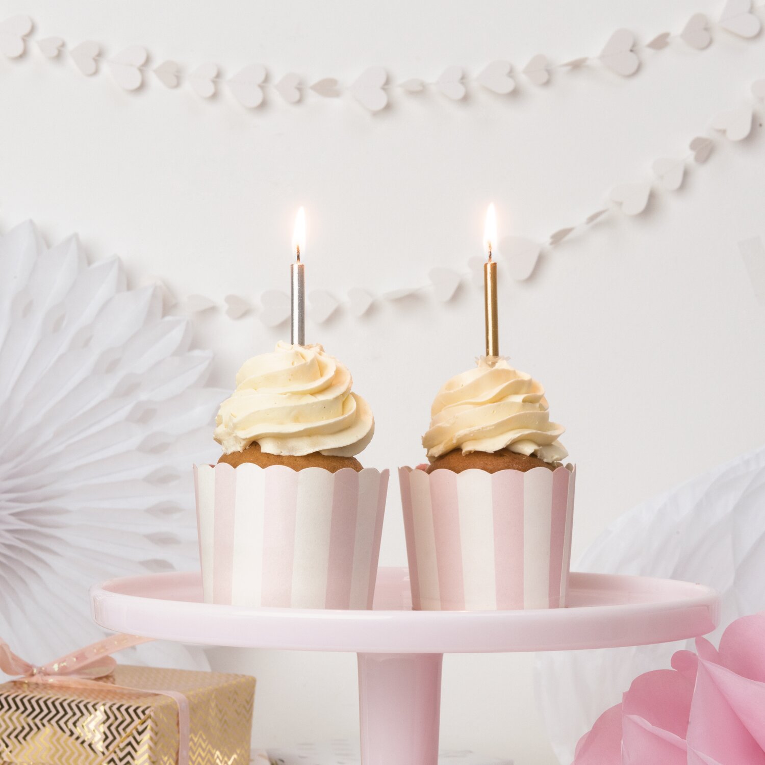 Kerzenset Gold-Silber, 48-teilig, von Rico Design auf Cupcakes mit brennenden Stabkerzen vor romantischer Partydeko mit Papierfächern und Girlande