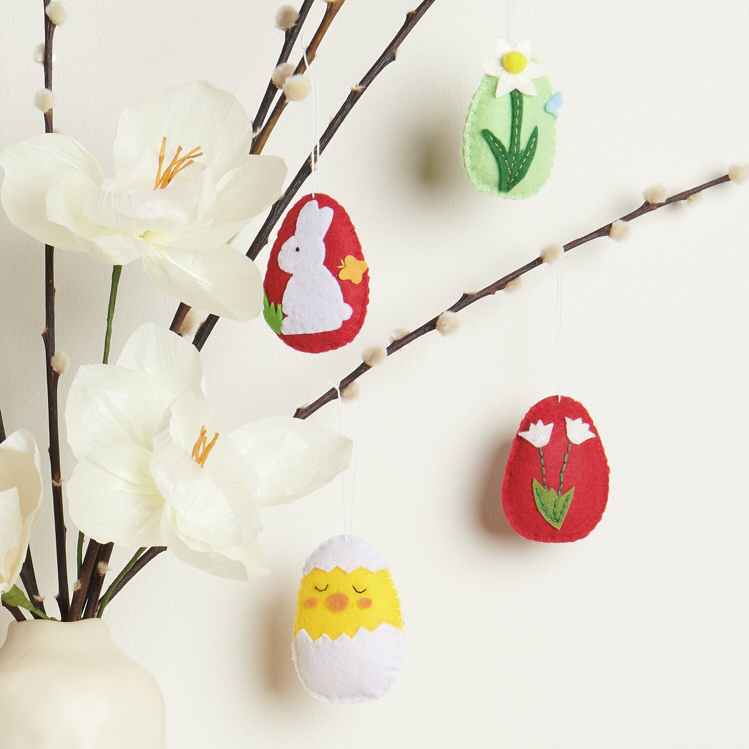 Aufhänger Filz-Osterei 2D 4 Stück: Bunte Filz-Ostereier mit Blumen- und Hasenmotiven an Zweigen dekoriert.