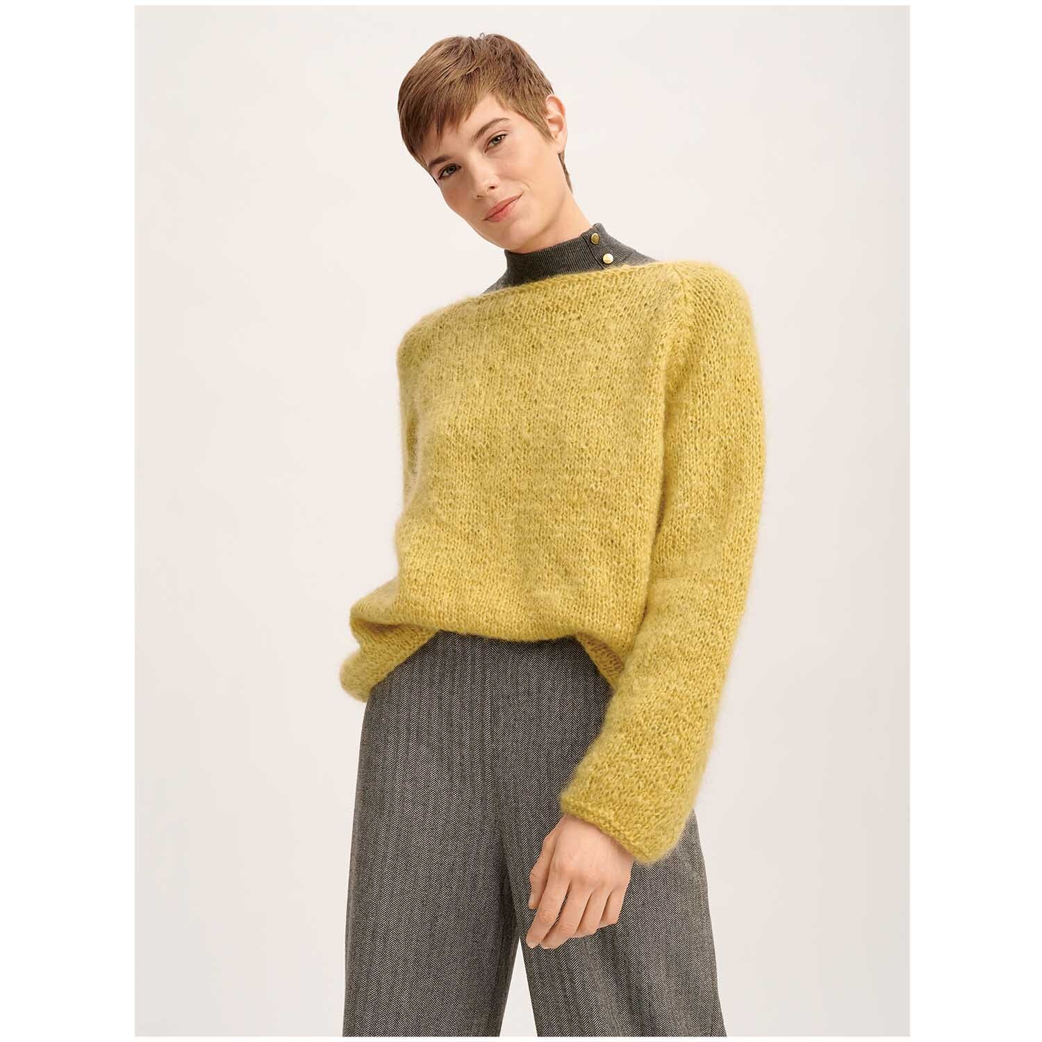 Fashion Mohair Merino Chunky: Person trägt einen senffarbenen Pullover von Rico Design, kombiniert mit grauer Hose.