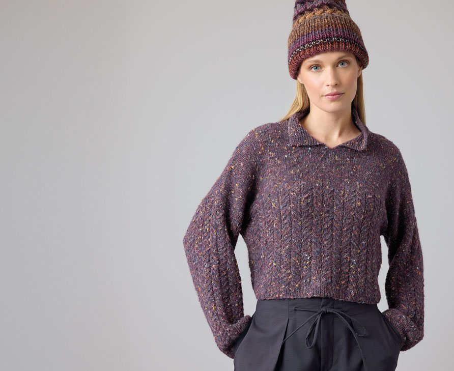 Frau trägt lilafarbenen Strickpulli und lilafarbene Strickmütze vor hellem Hintergrund