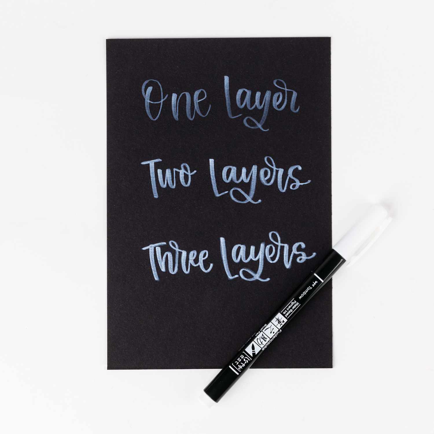 Fudenosuke Brush Pen Pastel von Tombow auf schwarzem Papier, zeigt Schrift in drei Schichten.