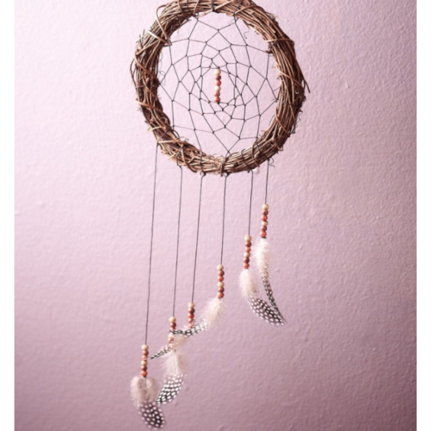 Kreative Traumfänger: Handgefertigter Traumfänger mit Federn und Perlen an rosa Wand hängend.