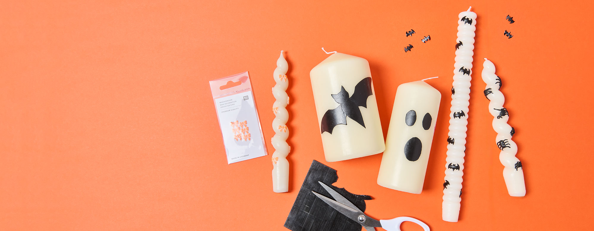 selbstgestaltete Kerzen mit Halloweenmotiven vor einem orangefarbenen Hintergrund.